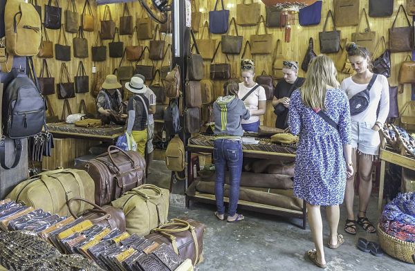 Leather shop in Hoi An shows wall and floor filled with leather bags as people try to decide what to buy.