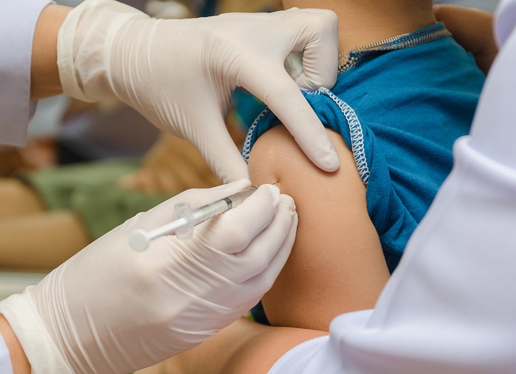 Medical professional wearing white gloved hands administering a vaccine injection into a patient's upper arm.