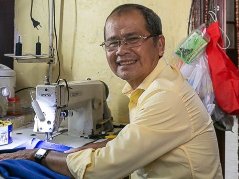 Mr Xe, one of the best and most friendly tailors in Hoi An smiles out from his sewing machine.