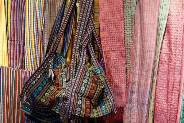 A handwoven bag surrounded by delicate silk scarves of plaid design in various colours show what tourists can buy in Vietnam