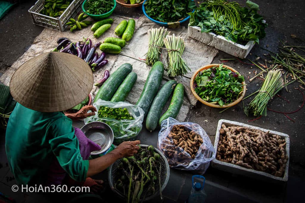 Aerial shot of Vietnamese seller in Conical hat selling green vegetables at Hoi An Market