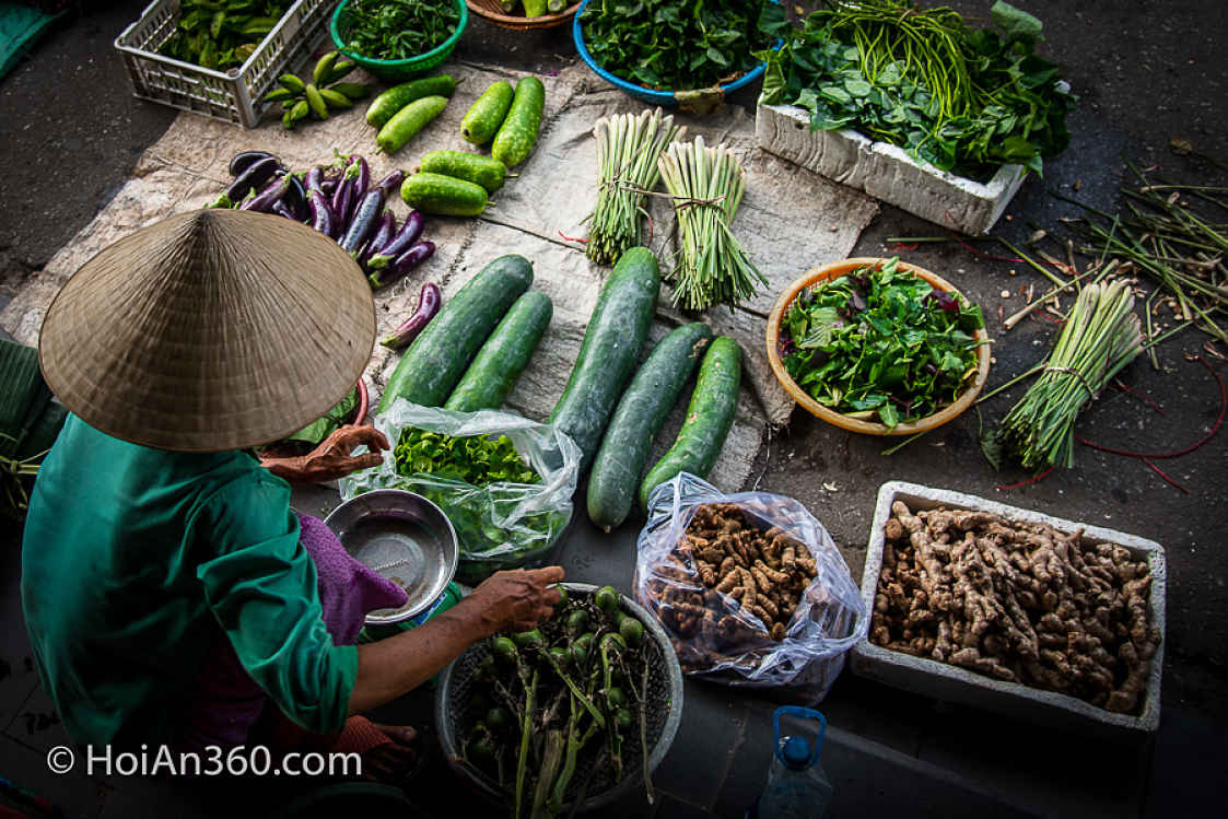 Aerial shot of Vietnamese seller in Conical hat selling green vegetables at Hoi An Market, Vietnam