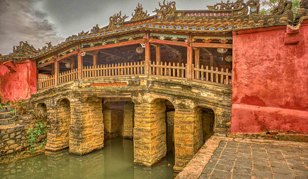 Japanese Bridge in Hoi An, bright red walls and ornate architecture with turrets and lanterns over a moat.