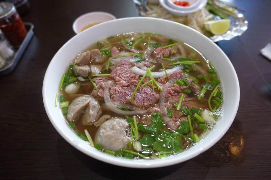 White dish of sliced rare beef, onions, corriander swimming in a rich brown broth is the most popular street food in Vietnam