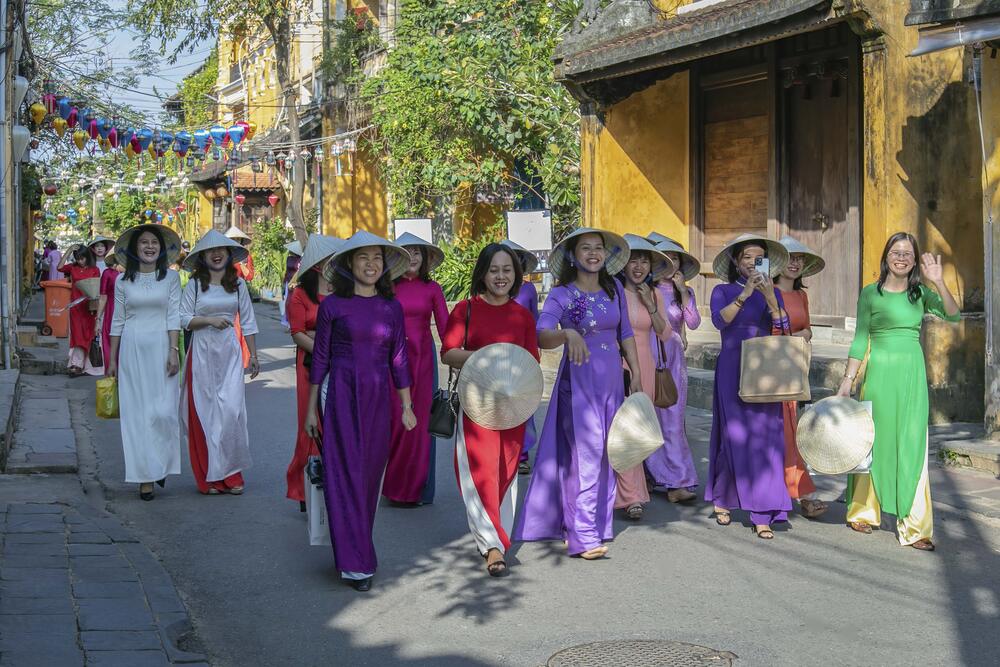 A large group of women strolling along Hoi An Ancient Town's streets in traditional Ao Dai