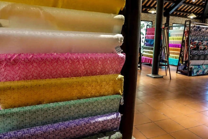 Bolts of colored silk hang from racks in a large warehouse style showroom to show the huge range of silk at Hoi An Silk Village