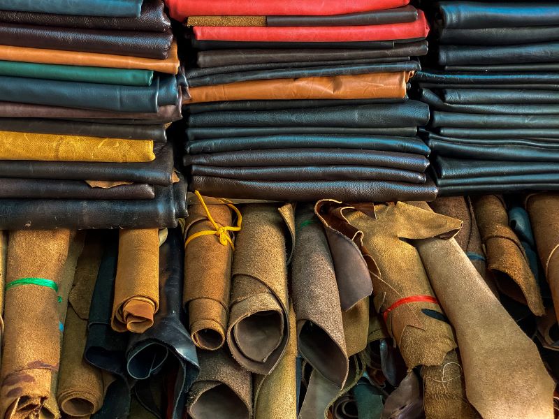 Piles of different colored leather on shelf and rolls of leather underneath shows the colour and type of leather available in Hoi An Leather shops