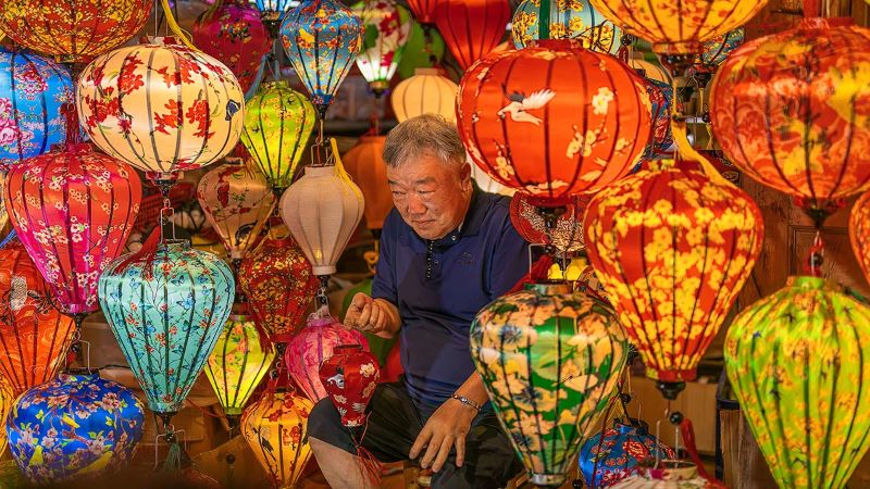 An old Korean man amongst masses of hanging lanterns posed to have his photo taken shows the many things to do at Hoi An Night Market