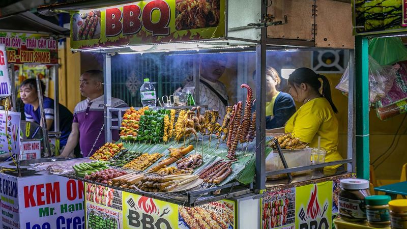 Vietnamese food stall sellers display in rows their skewered kebab style meats and fish for BBQ amid smoking pop up food stalls at Hoi An Night Market