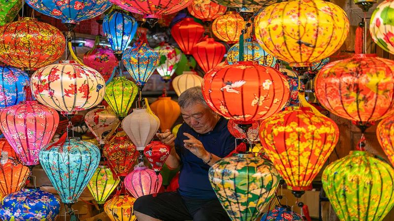 An old Korean man amongst masses of hanging lanterns posed to have his photo taken shows the many things to do at Hoi An Night Market